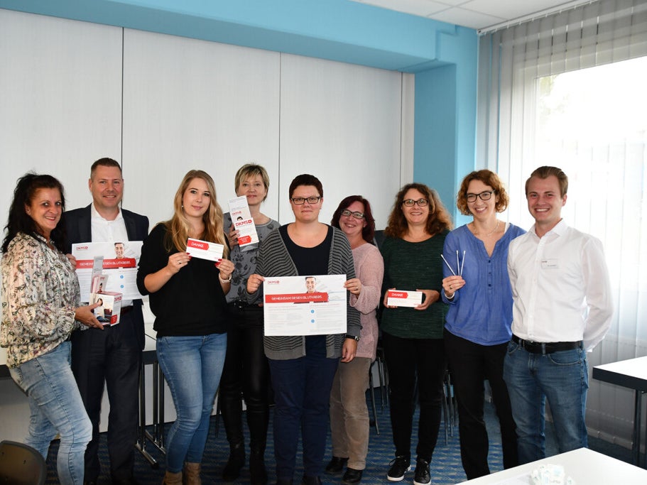 Eine Gruppe von Menschen hält Schilder, Registrierungssets und Wattestäbchen hoch Eine Gruppe von Menschen hält Schilder, Registrierungssets und Wattestäbchen hoch