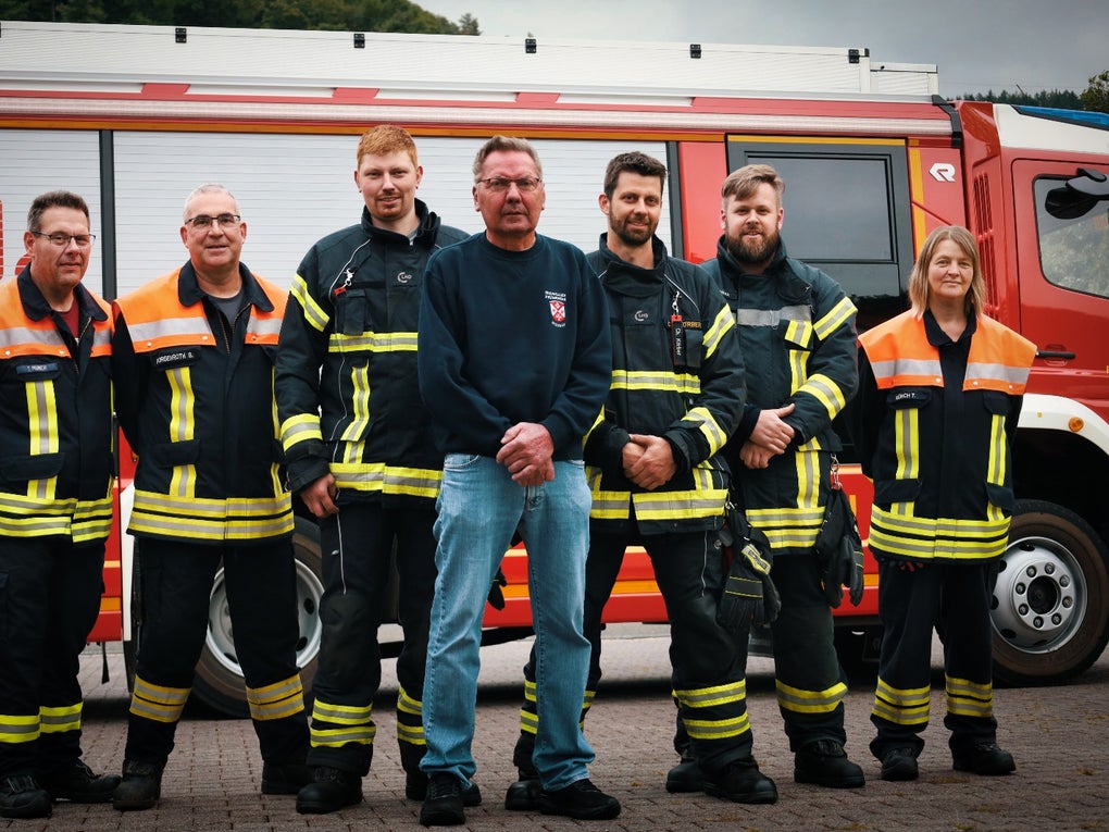Eine Gruppe von Feuerwehrleuten steht vor einem roten Lastwagen Eine Gruppe von Feuerwehrleuten steht vor einem roten Lastwagen