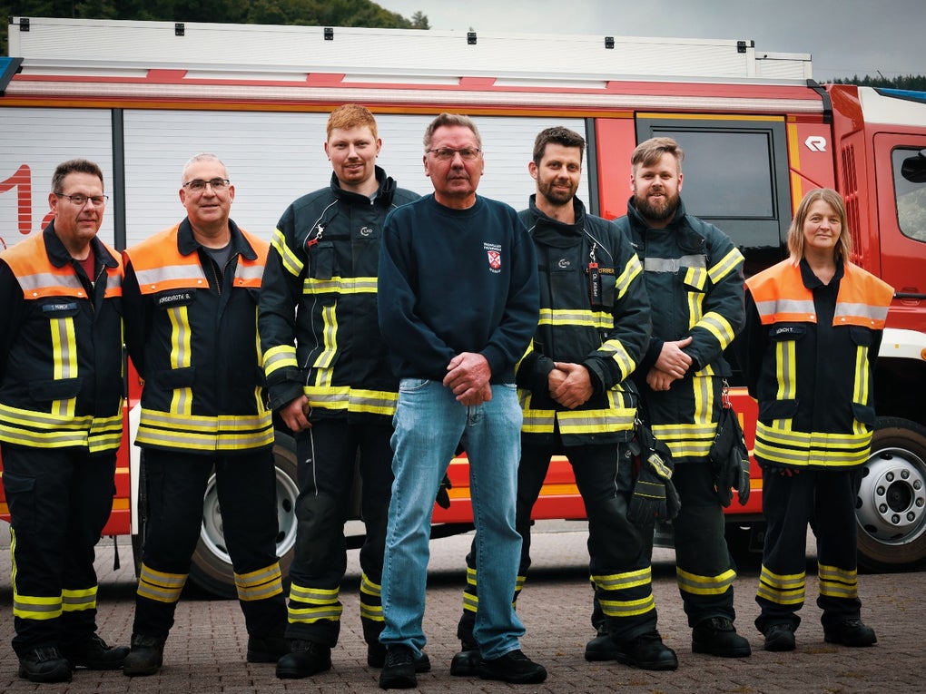 Eine Gruppe von Feuerwehrleuten steht vor einem roten Lastwagen Eine Gruppe von Feuerwehrleuten steht vor einem roten Lastwagen
