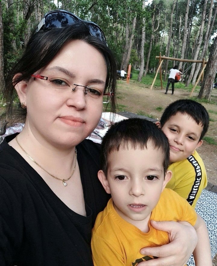 Özgül mit ihren zwei Kindern auf einem Spielplatz im Wald. 