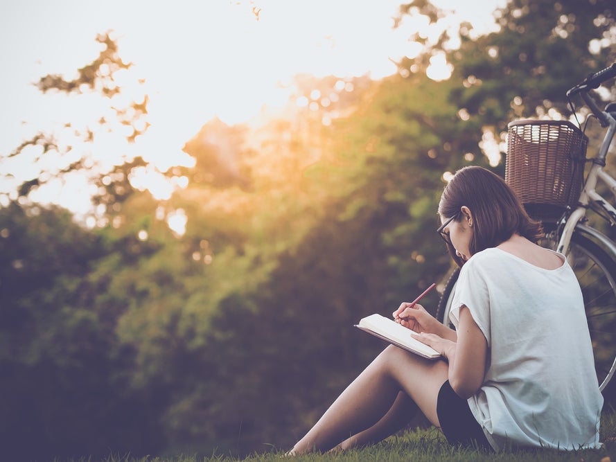 Eine Frau sitzt im Gras und schreibt in ein Notizbuch Eine Frau sitzt im Gras und schreibt in ein Notizbuch