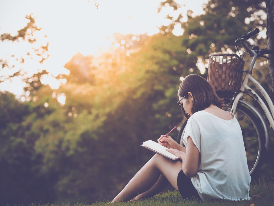 Eine Frau sitzt im Gras und schreibt in ein Notizbuch Eine Frau sitzt im Gras und schreibt in ein Notizbuch