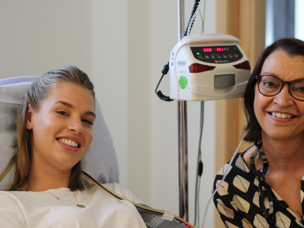 Eine Frau lächelt neben einer Frau in einem Krankenhausbett Eine Frau lächelt neben einer Frau in einem Krankenhausbett