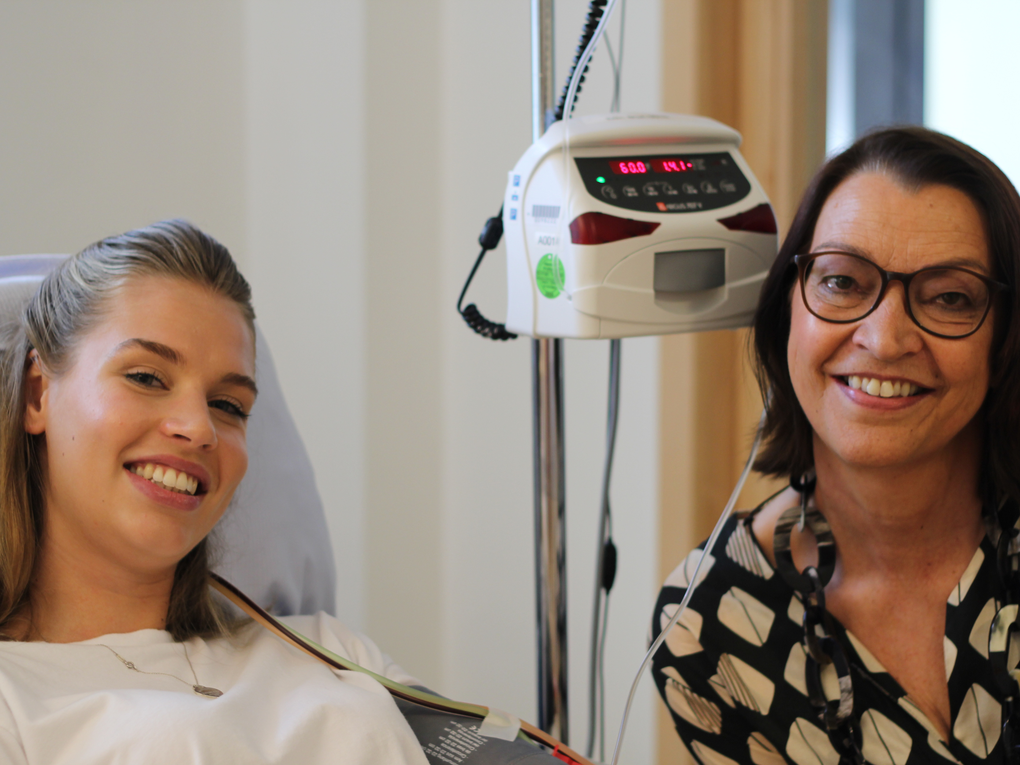 Eine Frau lächelt neben einer Frau in einem Krankenhausbett Eine Frau lächelt neben einer Frau in einem Krankenhausbett