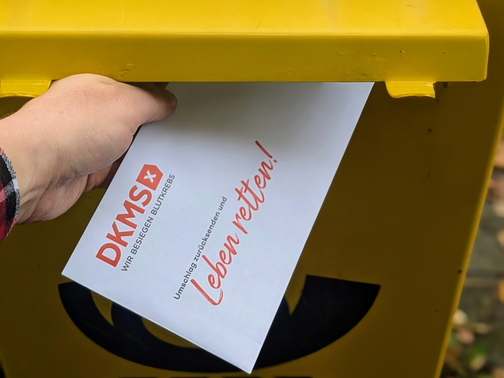 Eine Hand steckt ein Stück Papier in einen gelben Briefkasten. Eine Hand steckt ein Stück Papier in einen gelben Briefkasten.