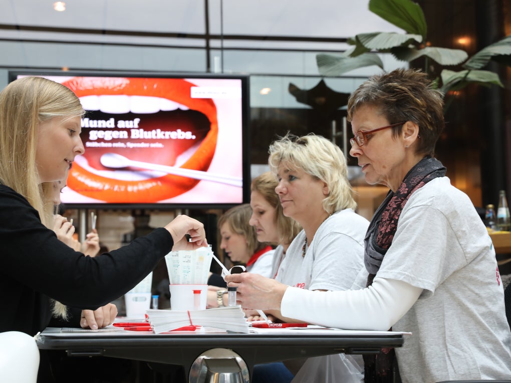 Eine Gruppe Frauen sitzt sich gegenüber. Im Hintergrund ist ein Display mit dem Text Mund auf gegen Blutkrebs. Eine Gruppe Frauen sitzt sich gegenüber. Im Hintergrund ist ein Display mit dem Text Mund auf gegen Blutkrebs.