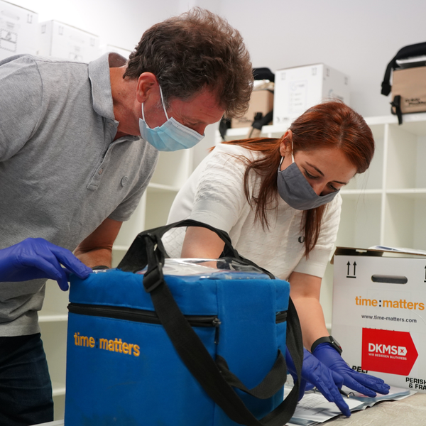 Foto von zwei Mitarbeiterinnnen - einer nimmt Stammzellen in einer Transportbox entgegen, die andere dokumentiert den Prozess Foto von zwei Mitarbeiterinnnen - einer nimmt Stammzellen in einer Transportbox entgegen, die andere dokumentiert den Prozess