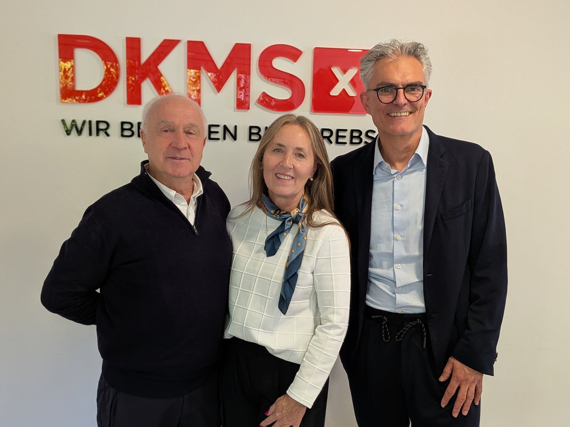 Eine Gruppe von Menschen posiert für ein Foto vor dem DKMS Logo Eine Gruppe von Menschen posiert für ein Foto vor dem DKMS Logo