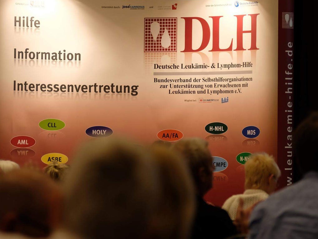Eine Gruppe von Menschen vor einem Plakat. Auf der linken Seite die Worte "Hilfe", Information, "Interessenvertretung". Auf der rechten Seite ein Logo Deutschen Leukämie- & Lymphom-Hilfe e.V. Eine Gruppe von Menschen vor einem Plakat. Auf der linken Seite die Worte "Hilfe", Information, "Interessenvertretung". Auf der rechten Seite ein Logo Deutschen Leukämie- & Lymphom-Hilfe e.V.