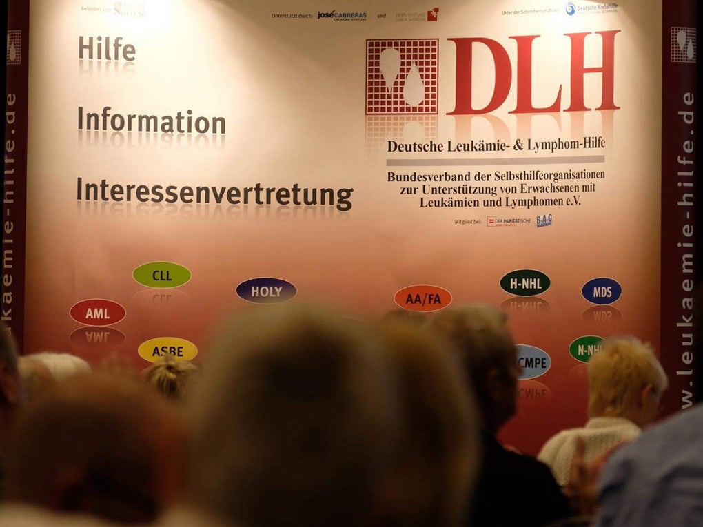 Eine Gruppe von Menschen vor einem Plakat. Auf der linken Seite die Worte "Hilfe", Information, "Interessenvertretung". Auf der rechten Seite ein Logo Deutschen Leukämie- & Lymphom-Hilfe e.V. Eine Gruppe von Menschen vor einem Plakat. Auf der linken Seite die Worte "Hilfe", Information, "Interessenvertretung". Auf der rechten Seite ein Logo Deutschen Leukämie- & Lymphom-Hilfe e.V.