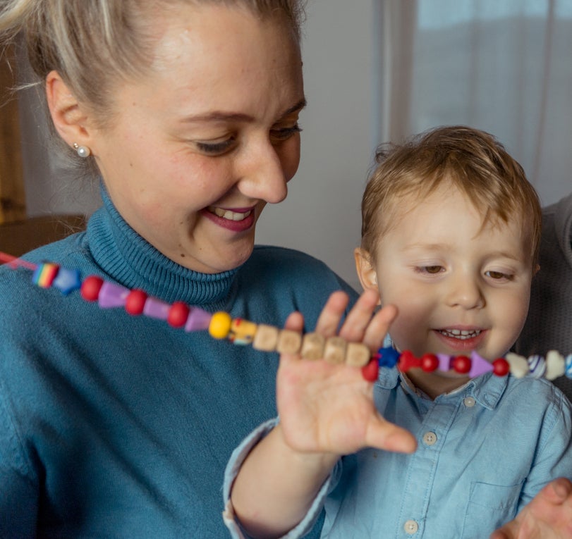 Patient Franz (3 J.) auf dem Schoß seiner Mutter. Beide lächeln und Franz greift nach einer selbstgebastelten Kette aus Holzperlen. Patient Franz (3 J.) auf dem Schoß seiner Mutter. Beide lächeln und Franz greift nach einer selbstgebastelten Kette aus Holzperlen.
