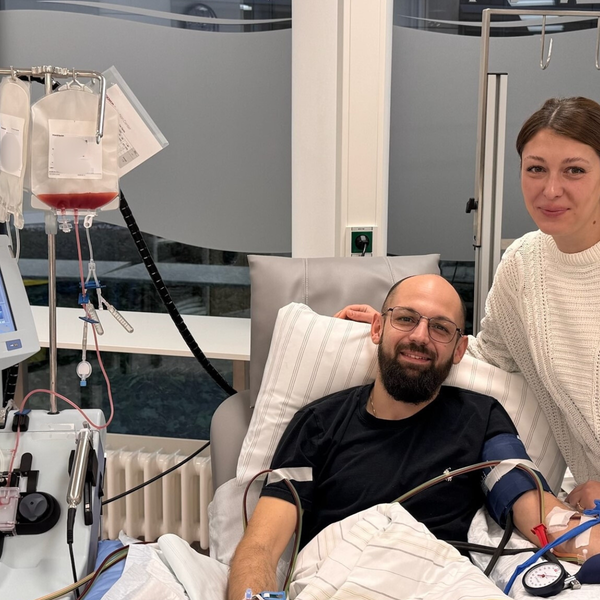 Pascal liegt in einem Krankenhausbett während der Stammzellenspende, Marie steht neben ihm Pascal liegt in einem Krankenhausbett während der Stammzellenspende, Marie steht neben ihm