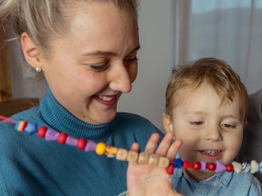 Eine Frau und ein Kind spielen mit Perlen, die auf einer Kette aufgefädelt sind. Eine Frau und ein Kind spielen mit Perlen, die auf einer Kette aufgefädelt sind.