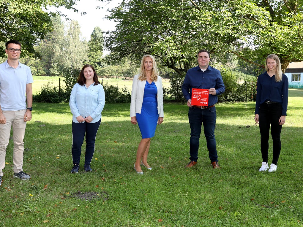 6 Menschen posieren auf einer Wiese für ein Foto, einer hält eine Tafel mit der Aufschrift: "Wir retten Leben" in der Hand 6 Menschen posieren auf einer Wiese für ein Foto, einer hält eine Tafel mit der Aufschrift: "Wir retten Leben" in der Hand