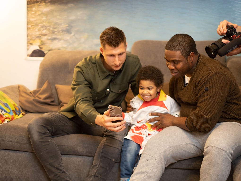 zwei Erwachsene sitzen mit einem Kind auf einem Sofa und gucken auf ein Handy zwei Erwachsene sitzen mit einem Kind auf einem Sofa und gucken auf ein Handy