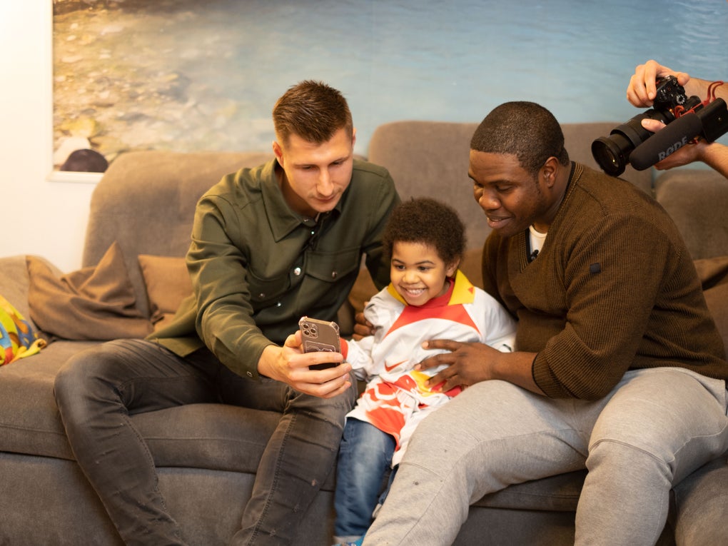 zwei Erwachsene sitzen mit einem Kind auf einem Sofa und gucken auf ein Handy zwei Erwachsene sitzen mit einem Kind auf einem Sofa und gucken auf ein Handy