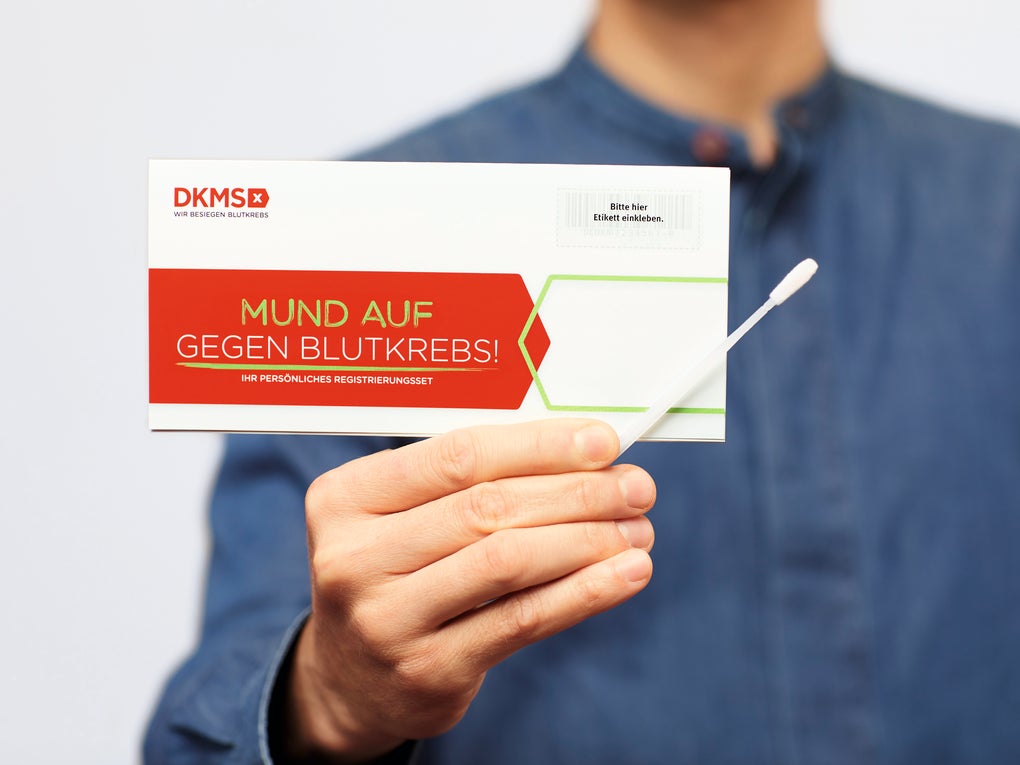 Eine Person mit einer Karte von der DKMS und einem Wattestäbchen in der Hand Eine Person mit einer Karte von der DKMS und einem Wattestäbchen in der Hand