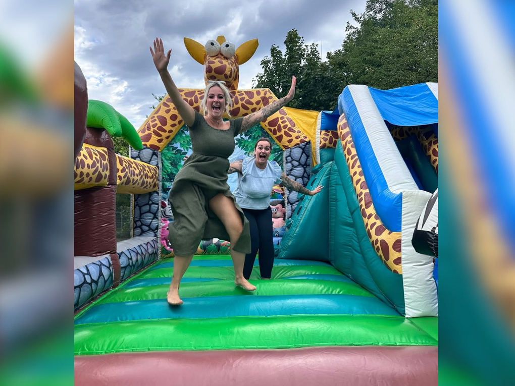 Zwei junge Frauen springen auf einer bunten Hüpfburg mit Giraffenkopf. Zwei junge Frauen springen auf einer bunten Hüpfburg mit Giraffenkopf.