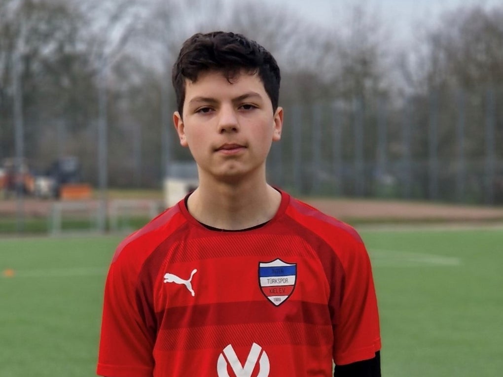 Ein Junge in einem roten Trikot, im Hintergrund sieht man einen Fußballplatz Ein Junge in einem roten Trikot, im Hintergrund sieht man einen Fußballplatz
