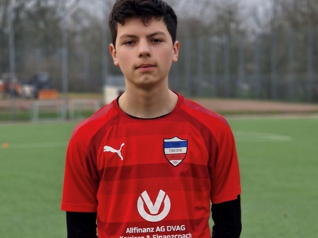 Ein Junge in einem roten Trikot, im Hintergrund sieht man einen Fußballplatz Ein Junge in einem roten Trikot, im Hintergrund sieht man einen Fußballplatz