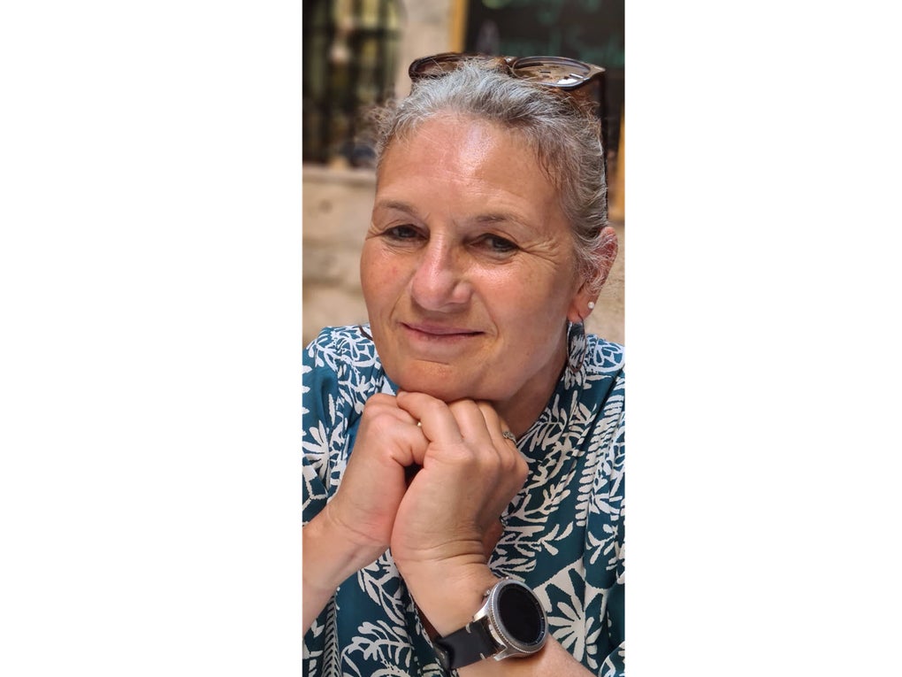 Eine Frau mit ergrautem Haar und einer auf dem Haar aufliegenden Brille stützt ihr Kinn auf den zu Fäusten geschlossenen Händen und lächelt. Eine Frau mit ergrautem Haar und einer auf dem Haar aufliegenden Brille stützt ihr Kinn auf den zu Fäusten geschlossenen Händen und lächelt.
