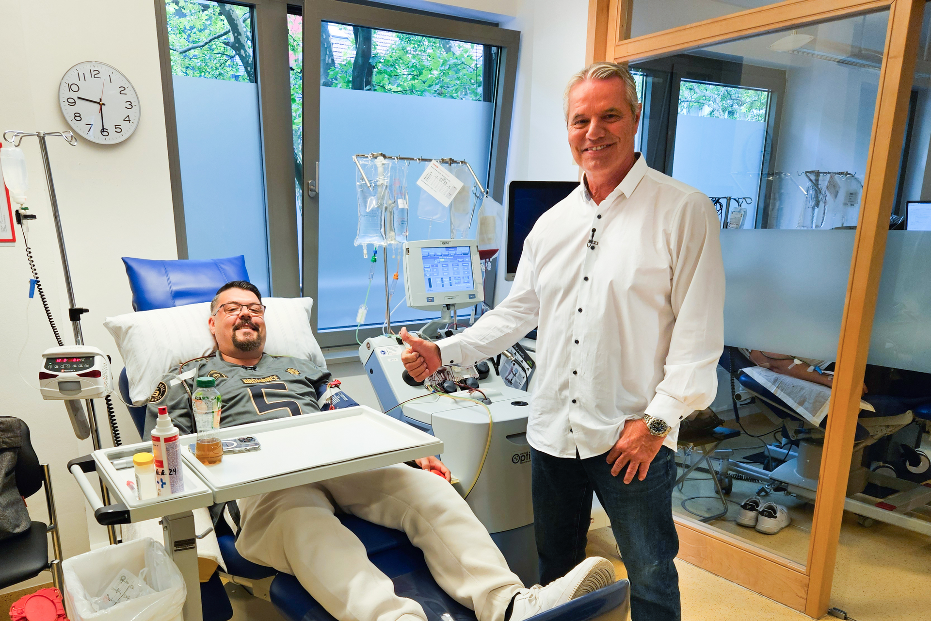 Ein Mann steht neben einem Mann in einem Krankenhausbett Ein Mann steht neben einem Mann in einem Krankenhausbett