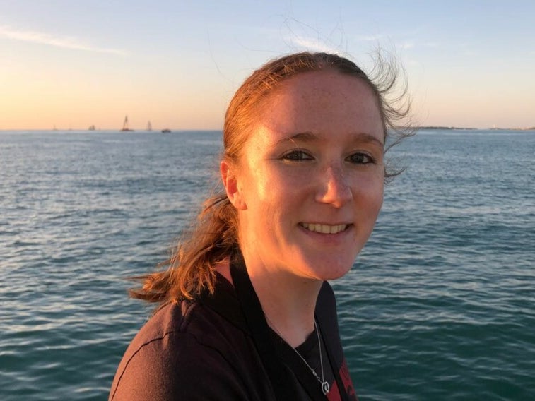 Eine Frau lächelt in die Kamera. Im Hintergrund sieht man Meer. Eine Frau lächelt in die Kamera. Im Hintergrund sieht man Meer.