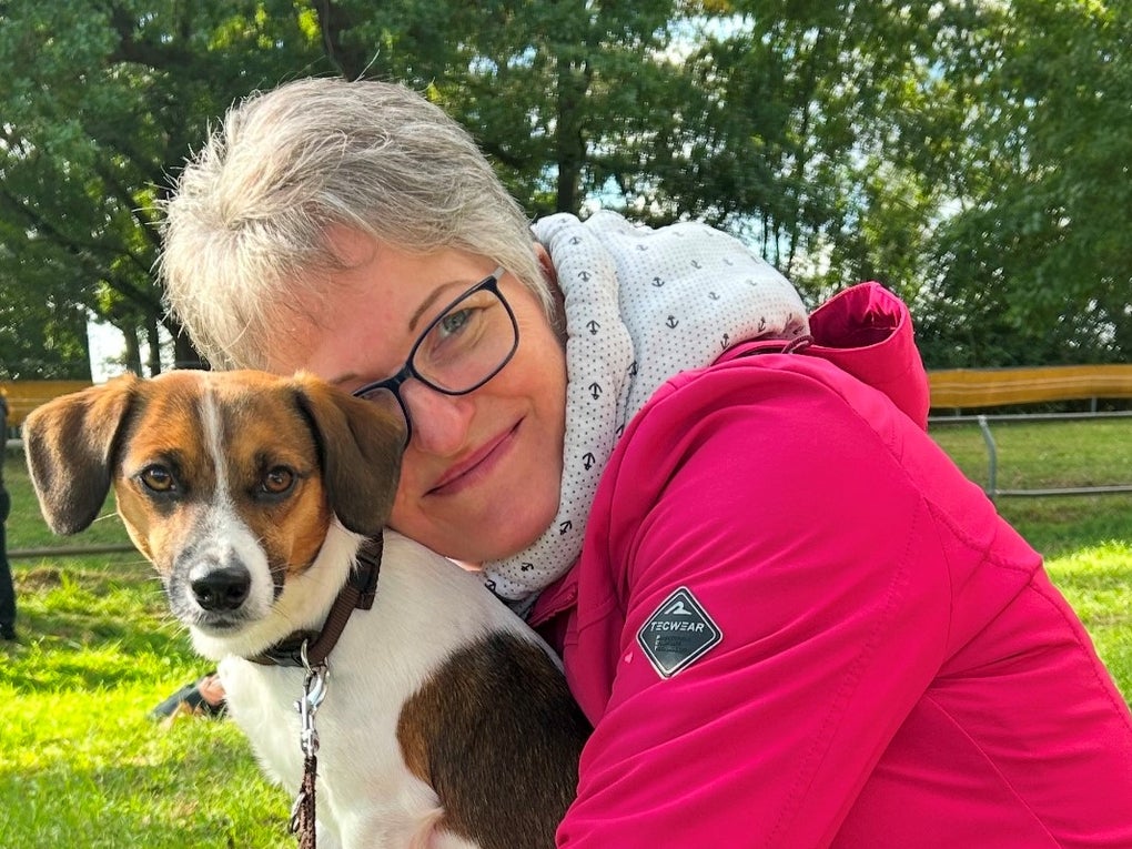 Eine Frau hält einen Hund, im Hintergrund sieht man einen Park Eine Frau hält einen Hund, im Hintergrund sieht man einen Park