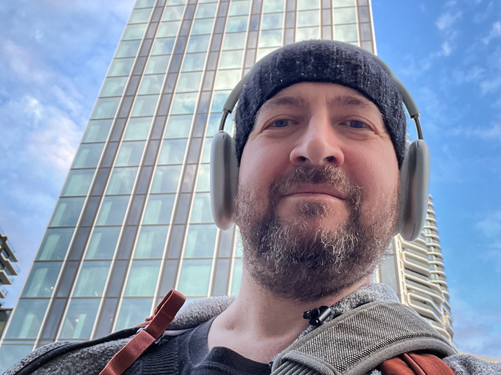 Ein Mann mit Kopfhörern und einer Mütze steht vor einem Hochhaus Ein Mann mit Kopfhörern und einer Mütze steht vor einem Hochhaus
