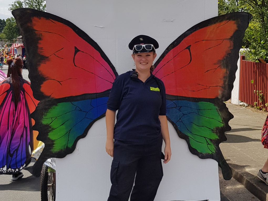 Eine Frau in Uniform steht vor einer Fotowand mit großen Schmetterlingsflügeln. Eine Frau in Uniform steht vor einer Fotowand mit großen Schmetterlingsflügeln.