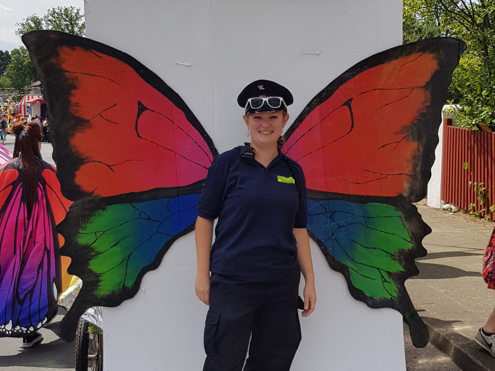 Eine Frau in Uniform steht vor einer Fotowand mit großen Schmetterlingsflügeln. Eine Frau in Uniform steht vor einer Fotowand mit großen Schmetterlingsflügeln.