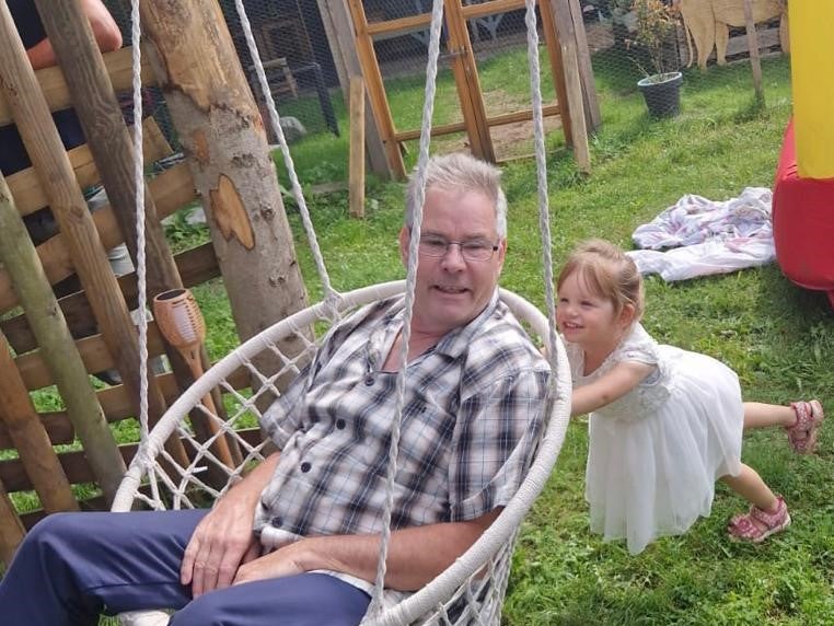 ein Mann sitzt in einer Schaukel während ein kleines Mädchen ihn anschubst ein Mann sitzt in einer Schaukel während ein kleines Mädchen ihn anschubst