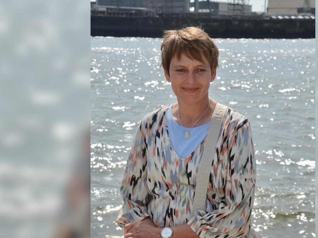 Eine Frau sitzt an einem Gewässer. Im Hintergrund ist ein Hafen zu sehen. Eine Frau sitzt an einem Gewässer. Im Hintergrund ist ein Hafen zu sehen.