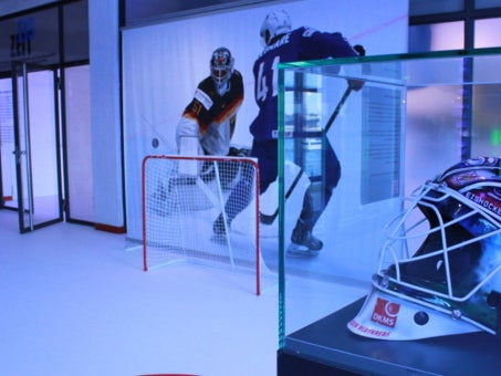Hockeyhelm in einer Vitrine auf einem Hockeyfeld mit Tor Hockeyhelm in einer Vitrine auf einem Hockeyfeld mit Tor