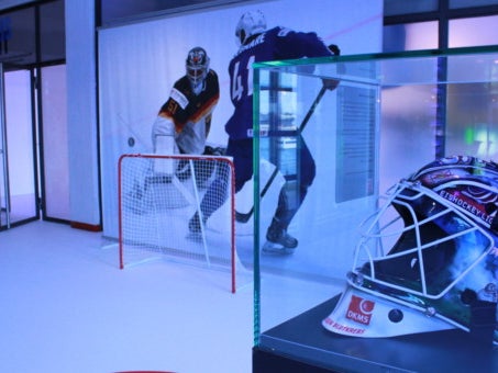 Hockeyhelm in einer Vitrine auf einem Hockeyfeld mit Tor Hockeyhelm in einer Vitrine auf einem Hockeyfeld mit Tor