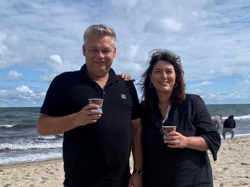 Ein Mann und eine Frau stehen an einem Strand und halten Tassen mit Kaffee Ein Mann und eine Frau stehen an einem Strand und halten Tassen mit Kaffee