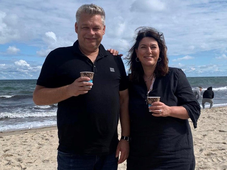 Ein Mann und eine Frau stehen an einem Strand und halten Tassen mit Kaffee Ein Mann und eine Frau stehen an einem Strand und halten Tassen mit Kaffee