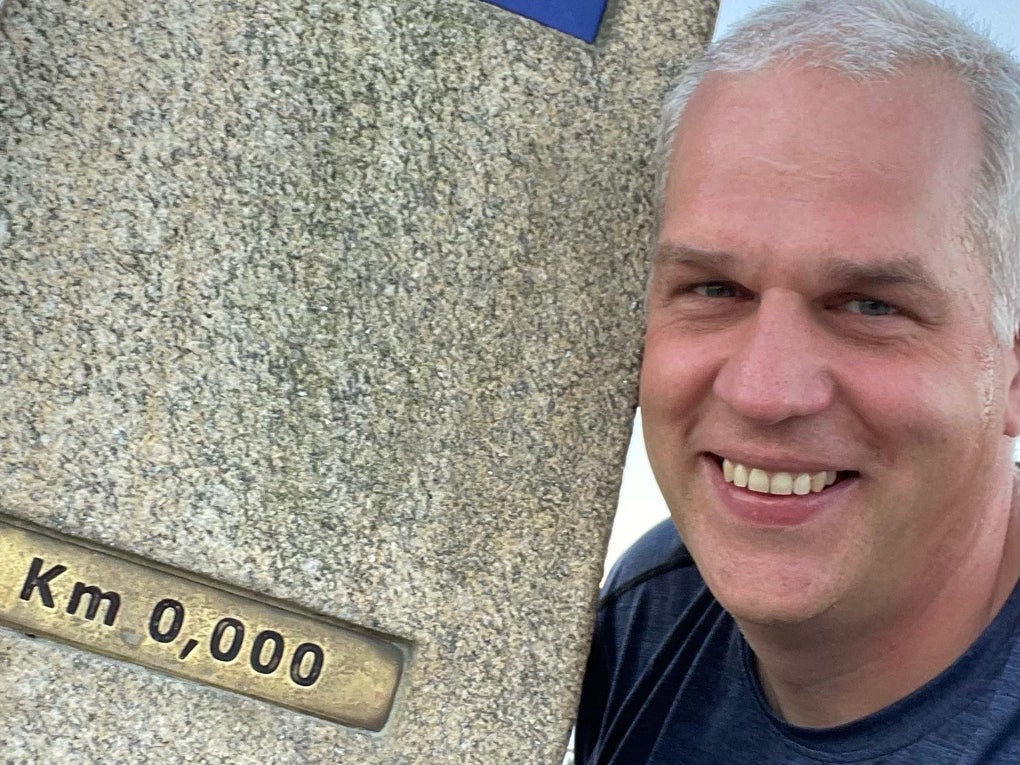 Markus lehnt an einem Pilgerwegmarker und lächelt in die Kamera. Markus lehnt an einem Pilgerwegmarker und lächelt in die Kamera.