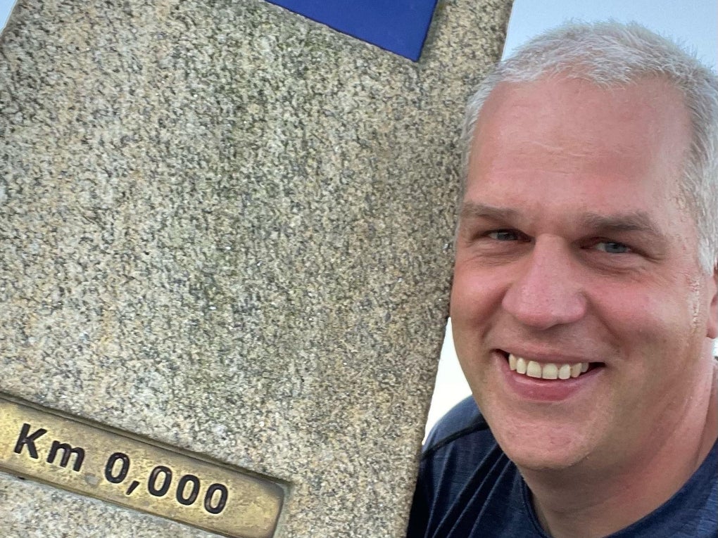 Markus lehnt an einem Pilgerwegmarker und lächelt in die Kamera. Markus lehnt an einem Pilgerwegmarker und lächelt in die Kamera.