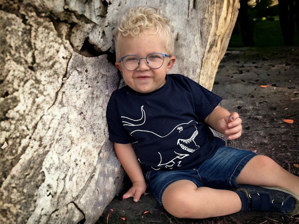 kleines Kind mit blonden Haaren und Brille sitzt auf dem Boden und lehnt an einen Baum kleines Kind mit blonden Haaren und Brille sitzt auf dem Boden und lehnt an einen Baum