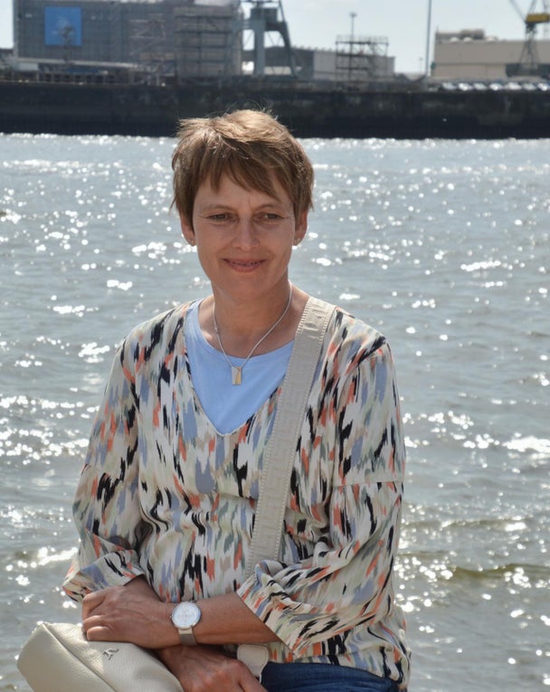 Patientin Beatrix sitzt vor einem Fluss in der Sonne und lächelt Patientin Beatrix sitzt vor einem Fluss in der Sonne und lächelt