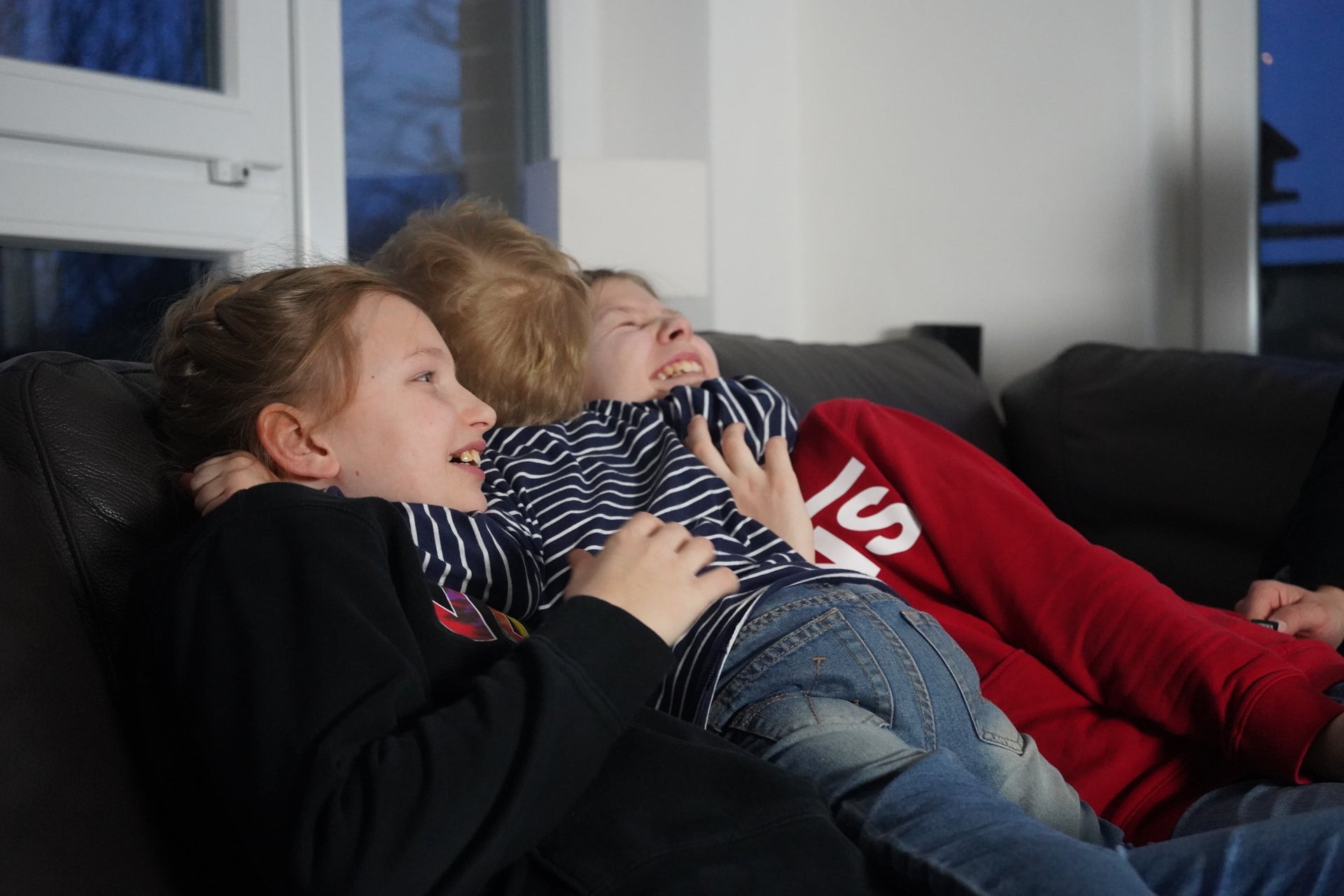 drei Geschwister liegen auf einem Sofa und lachen drei Geschwister liegen auf einem Sofa und lachen