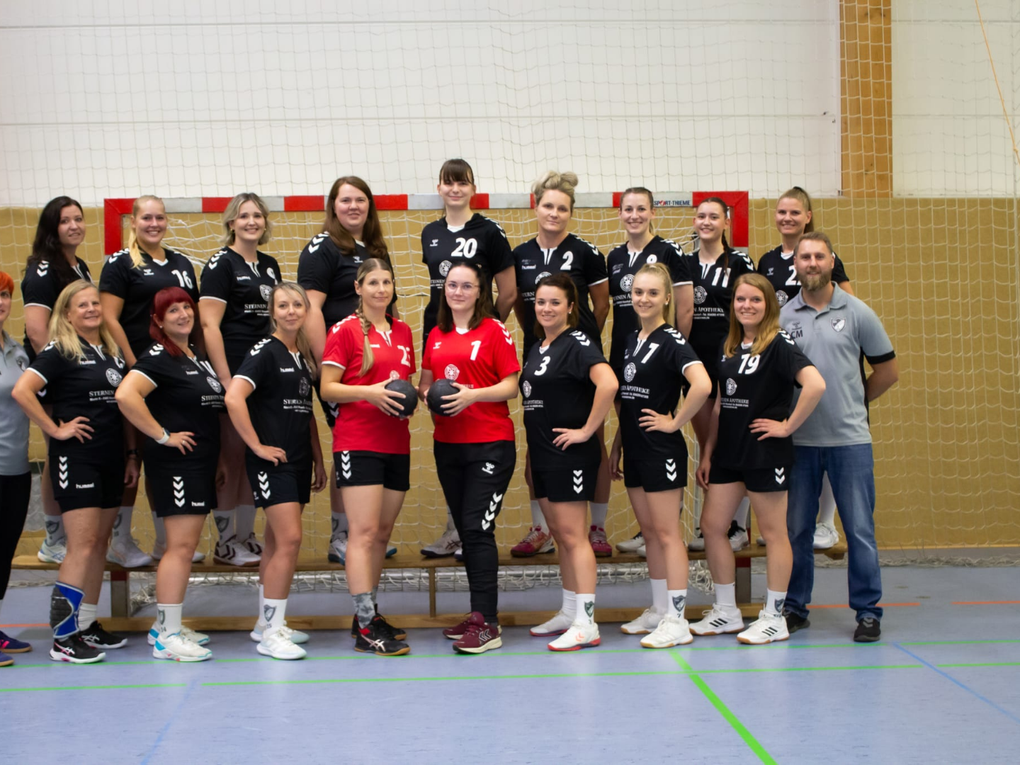 Eine Damenhandballmannschaft steht mit zwei Trainer:innen vor einem Tor. Eine Damenhandballmannschaft steht mit zwei Trainer:innen vor einem Tor.