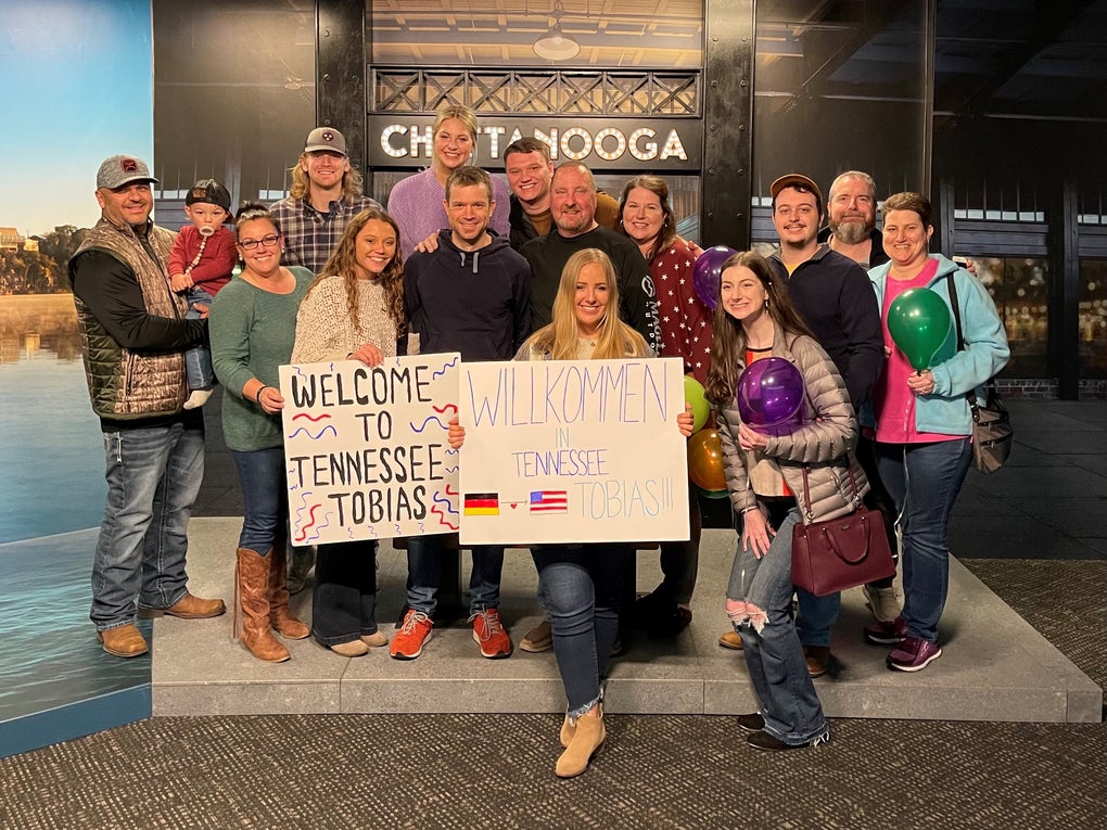 Eine Gruppe von Menschen posiert für ein Foto, sie halten Wilkommens-Schilder hoch Eine Gruppe von Menschen posiert für ein Foto, sie halten Wilkommens-Schilder hoch