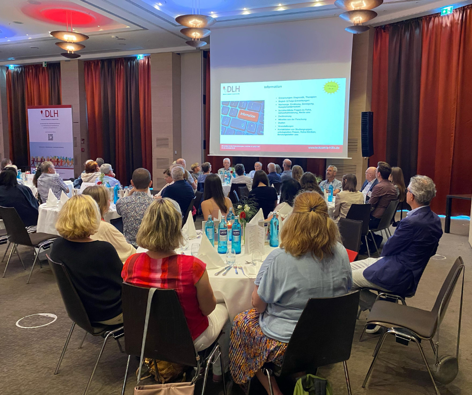 Eine Gruppe von Personen, die an einem Tisch vor einer Projektionsfläche sitzen Eine Gruppe von Personen, die an einem Tisch vor einer Projektionsfläche sitzen