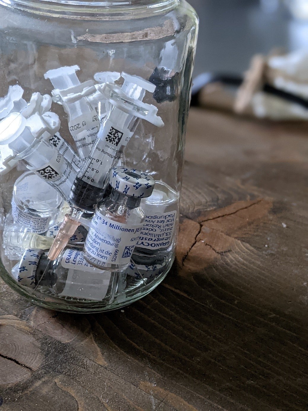 Ein Glasgefäß mit Spritzen und Fläschchen auf einer Holzfläche Ein Glasgefäß mit Spritzen und Fläschchen auf einer Holzfläche
