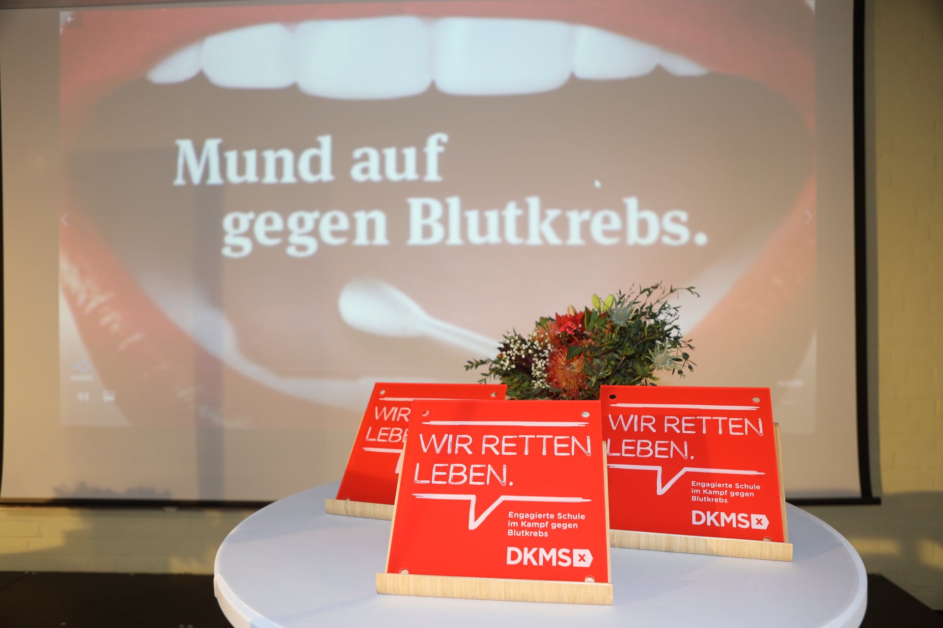 drei DKMS Schulsiegel mit einem Blumenstrauß auf einem Tisch drei DKMS Schulsiegel mit einem Blumenstrauß auf einem Tisch