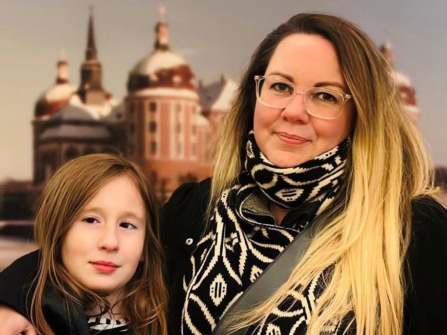 Eine Frau mit Brille und Schal legt ihren Arm um ein Mädchen. Eine Frau mit Brille und Schal legt ihren Arm um ein Mädchen.