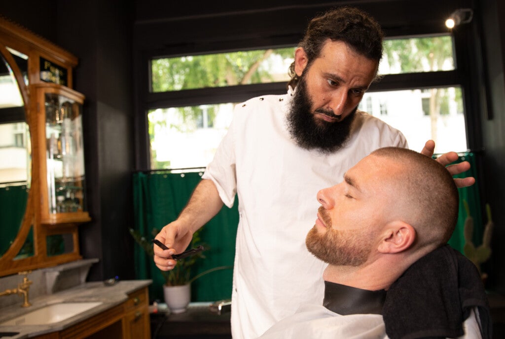 Ein Mann in einem weißen Hemd rasiert den Kopf von Daniel Korte Ein Mann in einem weißen Hemd rasiert den Kopf von Daniel Korte