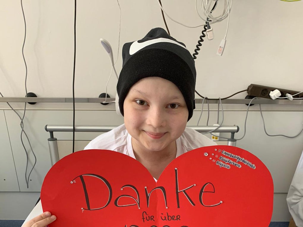 Lana sitzt im Schneidersitz auf einem Bett und hält ein Schild: "Danke für über 10 Tausend Wangenabstriche" Lana sitzt im Schneidersitz auf einem Bett und hält ein Schild: "Danke für über 10 Tausend Wangenabstriche"